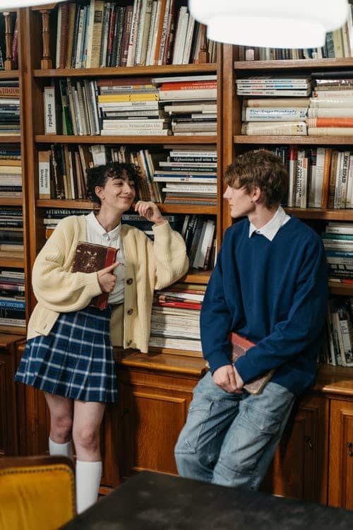 College Students Looking at Each Other while Leaning on Bookcase